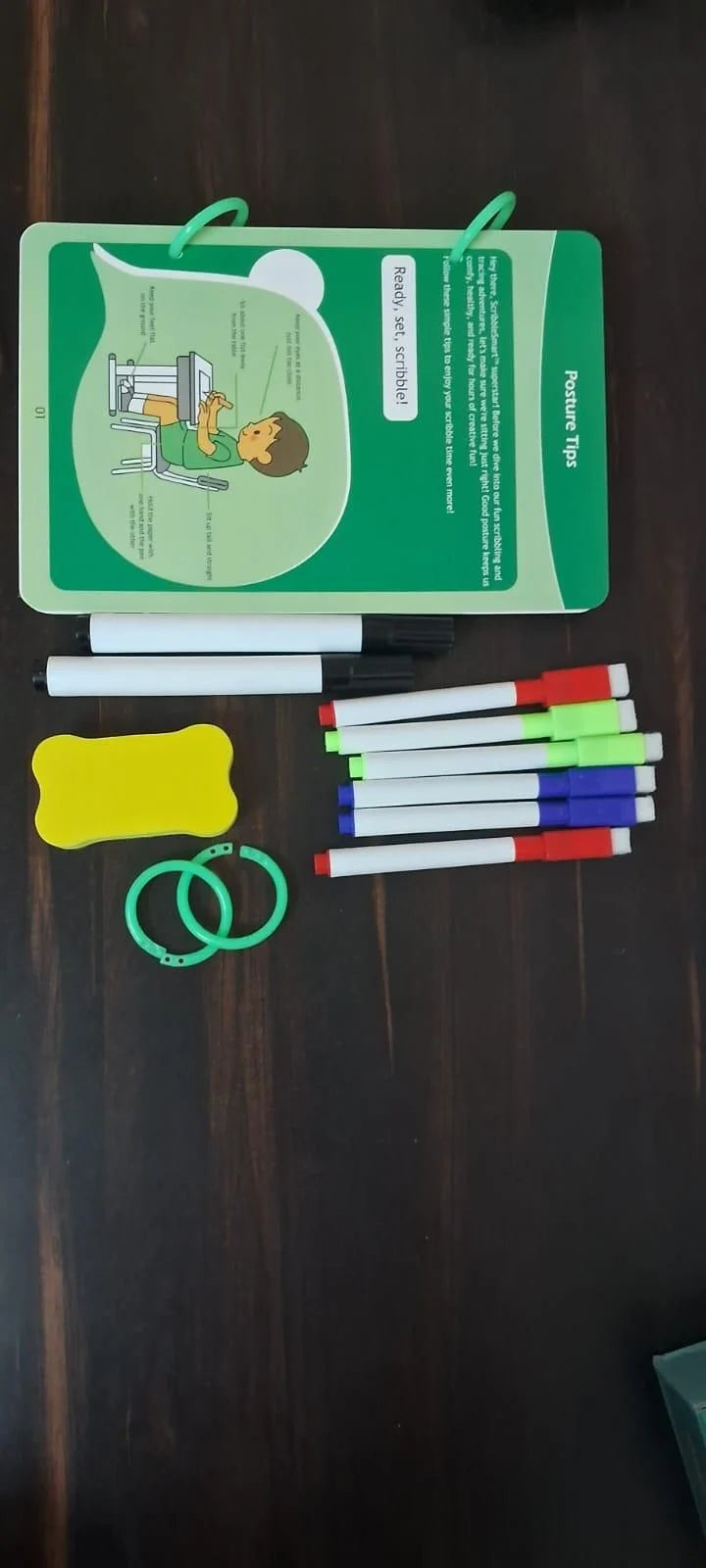 Educational materials including a book, markers, and other stationery items on a dark surface.