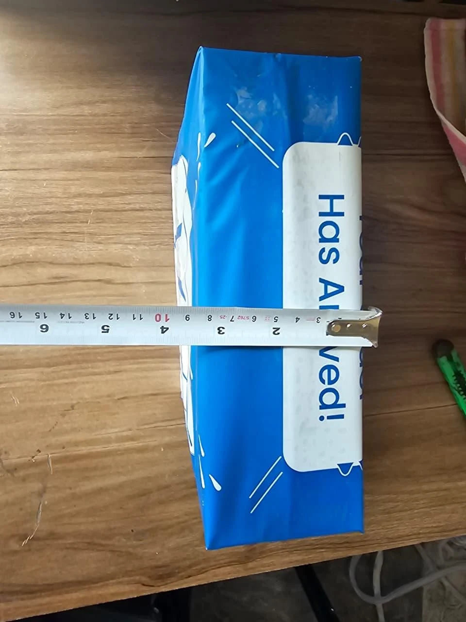 Blue package with 'Has Alived!' text on a wooden surface, measured by a ruler.